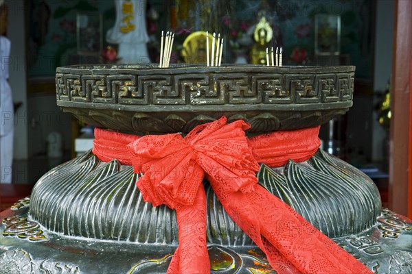 Red ribbon on a bowl for incense sticks in front of a pagoda
