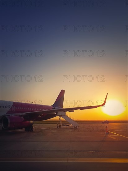 Airplane ready for boarding and takeoff at the airport with the view to the sunrise. Morning travel and holiday concept