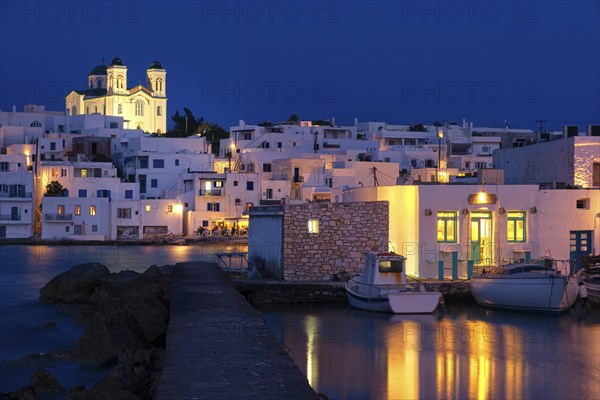 Traditional Greek whitewashed houses and church of Dormition of Mother of God on hilltop by seafront after sunset
