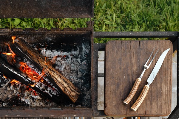 Top view of metal grill with burning log and fork and knife for steak
