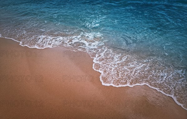 Serene blue sea with foamy waves hits the sandy shore. Beach and water texture