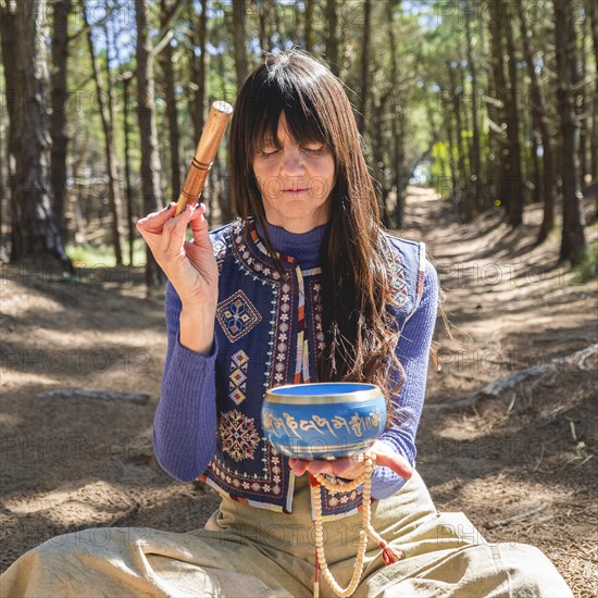 Close up of a woman playing a Tibetan singing bowl in the woods