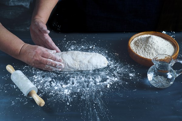 Woman kneading with her hands a flour dough to make homemade bread on a black wooden table with flour
