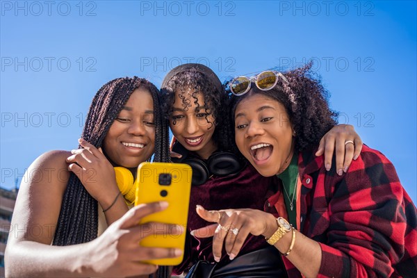 Low angle view of three multi-ethnic friends smiling while sharing a mobile outdoors