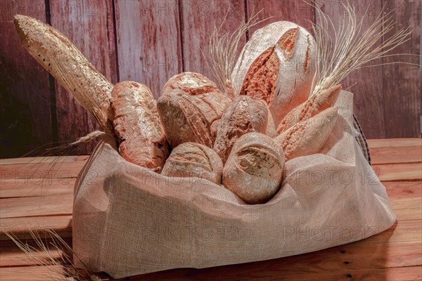 Different types of seed bread in a raffia sack on a wooden table with ears of wheat