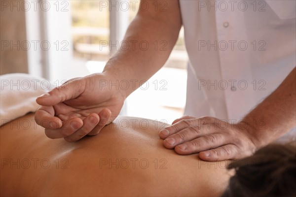 Detail shot of a masseur's hands treating the back of a woman lying on a massage table in a clinic