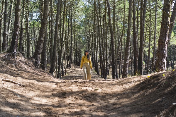 Adult woman walking over a path under the trees in the forest