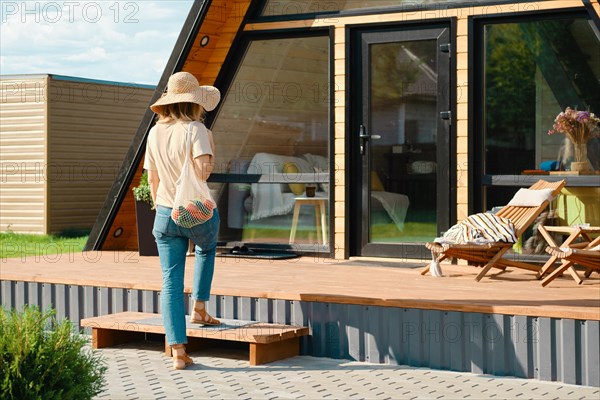 Adult woman returns from the farmer market to her wooden cabin