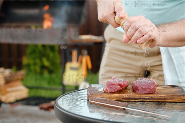 Unrecognizable man using hand mill to season raw strip steak with salt