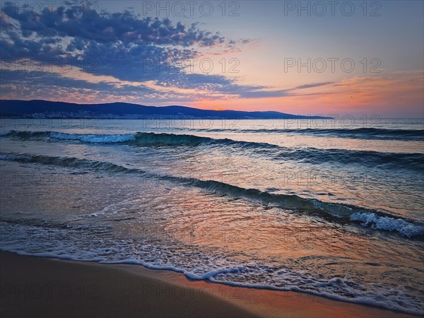 Sunrise at the sea with foamy waves on the sand and colorful sky at the horizon. Summer and travel background