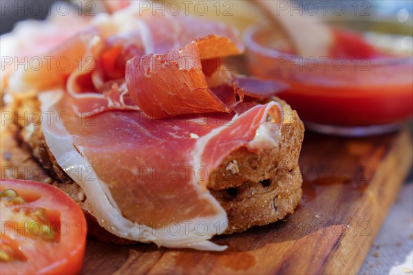 Close-up of a typical Spanish acorn-fed iberian ham and tomato toast on a wooden board with a bowl of freshly crushed tomatoes