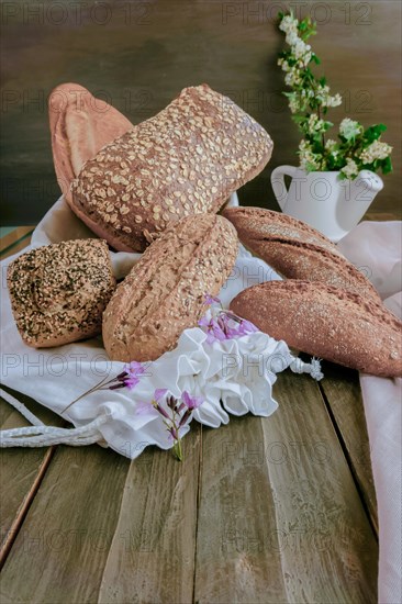 Different types of handmade rustic bread made of seeds on a pink cloth on a wooden table decorated with flowers