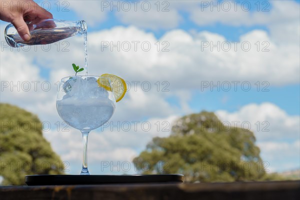 Woman's hand pouring tonic from a bottle into a glass with ice