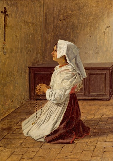 A woman prays on her knees in front of a cross on the wall