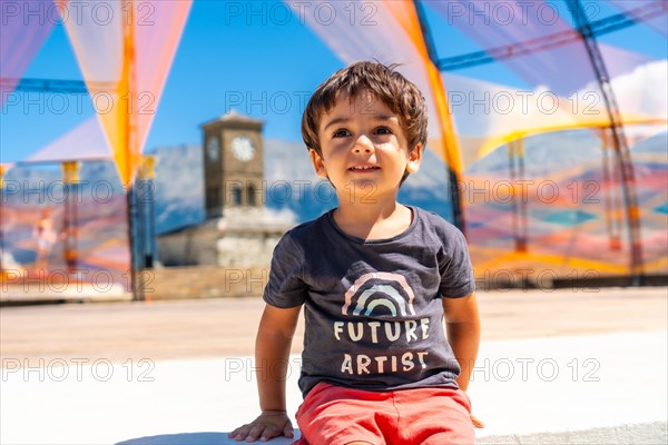 Portrait of a child in the colorful arches in the Ottoman Castle Fortress of Gjirokaster or Gjirokastra and in the background the church with the clock tower. Albania