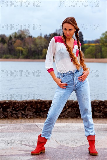 Young woman with long hair on the lakeshore in jeans and rubber boots