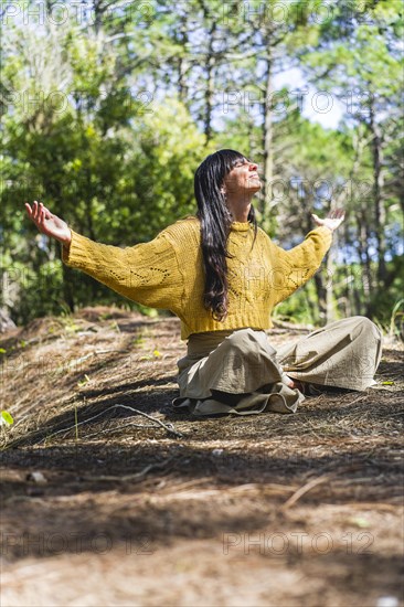 Woman sitting on the woods with arms opened while looking to the sky like thanking God. Vertical shot