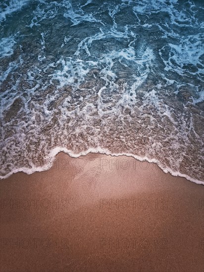 Soft foaming wave of the blue sea hits the sandy shore. Beach and water texture