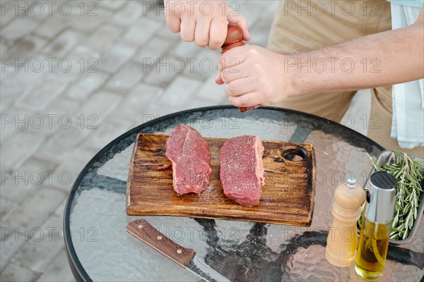 Top view of unrecognizable man seasoning raw beef steak with pepper preparing meal for grill