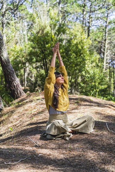 Woman about to meditate with hands clasped to the sky on the woods. Vertical shot