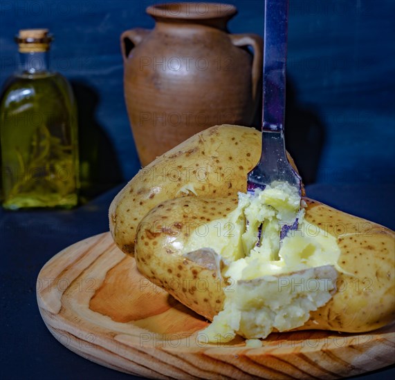 Boiled potato opened with a fork on a wooden plate