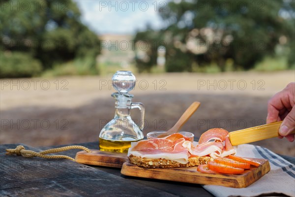 Woman putting slices of acorn-fed iberian ham on a slice of bread with tomato and olive oil on a wooden table in the countryside