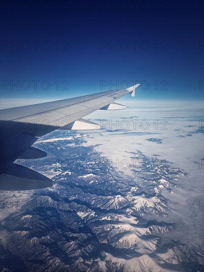 Plane flight above the Carpathian Mountains snowy peaks. Blue skyline and airplane wing seen through the window