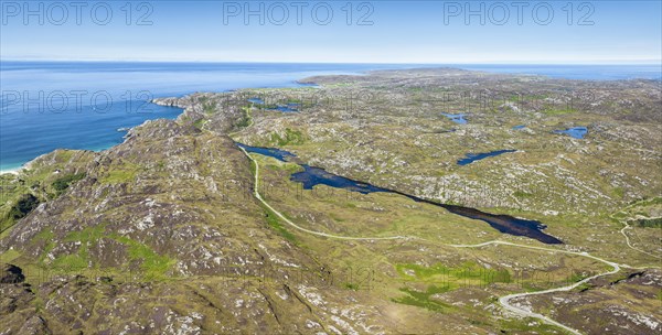 Aerial panorama of the sparsely populated North West Highlands with the single track road and pass road B869 running along the freshwater loch at Ordain. On the horizon the Atlantic Ocean