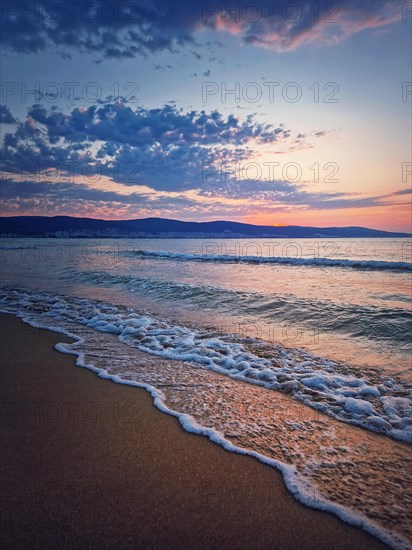 Sunrise at the sea with foamy waves on the sand and colorful sky at the horizon. Summer and travel background