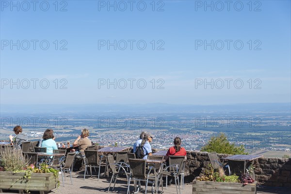 Tourists at the viewpoint in front of the Chateau du Haut Koenigsbourg. In the background the Upper Rhine Plain and the hilly landscape of the Black Forest