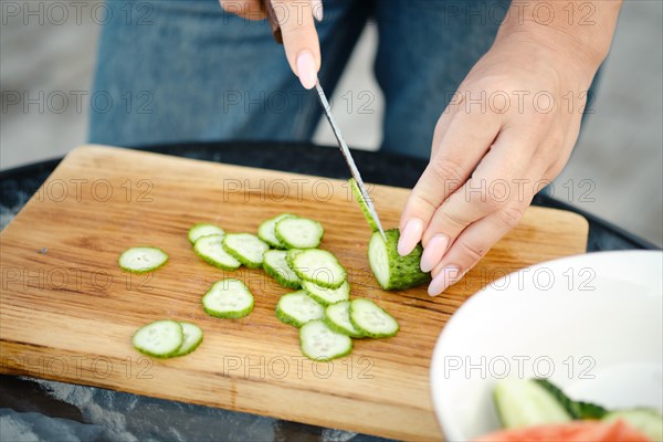 Unrecognizable woman slicing fresh cucumber for salad