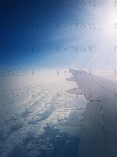 Plane flight above the clouds. Blue skyline and airplane wing seen through the window