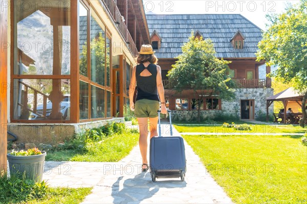 Tourist woman with a suitcase on rural vacation arriving at a mountain cabin
