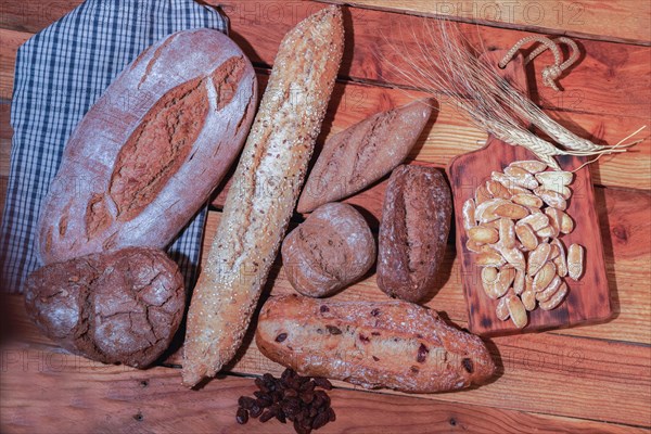 Top view of an assortment of rustic breads of different seeds and flours on a wooden table with ears of wheat