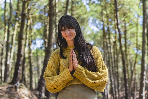 Smiling woman clasping hands while looking at camera outdoors