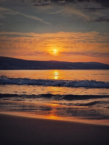 Early morning at the beach with vibrant sunrise at horizon and foamy waves hitting the sand. Dawn at the sea