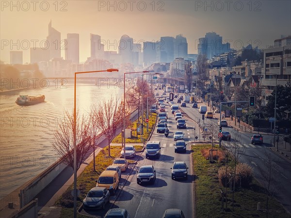 Busy traffic on highway and city streets creating high pollution and smog. Urban sunset view across Seine river to La Defense metropolitan district