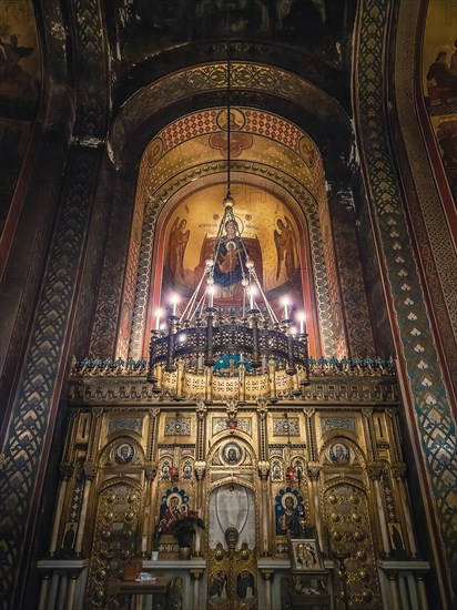 Interior details of Curtea de Arges monastery. The altar and ornate walls with painted icons and a golden chandelier with lights suspending out of ceiling