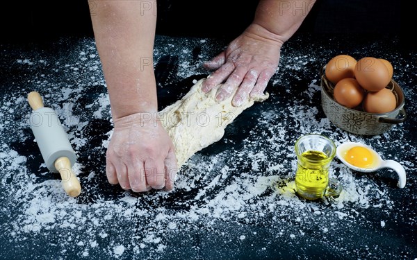 Woman kneading bread dough with her hands on a black wooden table with olive oil