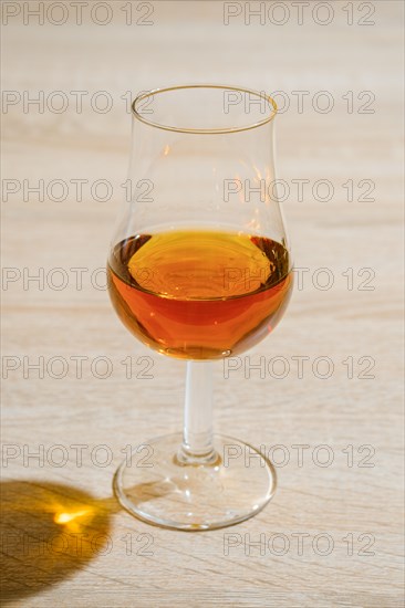 Tulip glass with cognac on wooden table under hard sunlight