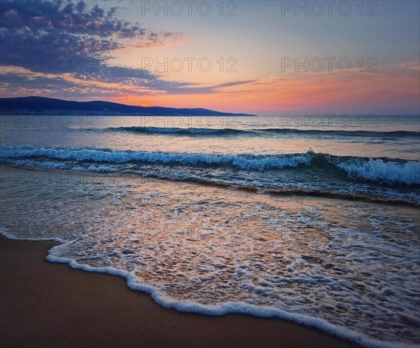 Dawn at the sea with foamy waves on the sand and colorful sky at the horizon. Sunny Beach coastline in Bulgaria. Summer and travel background