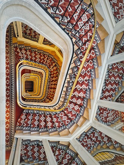 Abstract shape luxurious stairs with red carpet cover and golden handrail. Hypnotic pattern swirl staircase with mirror reflections on the stairwell walls