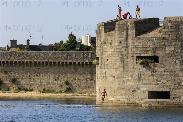 Young people jump from the wall of the fortress surrounding the old town of Ville close into the water of the harbour of Concarneau