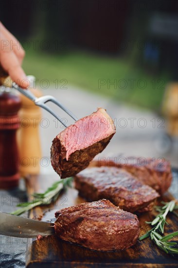 Unrecognizable man holds piece of grilled strip steak on the fork