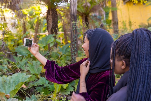 Rear view of a muslim woman taking a selfie with friends in a park