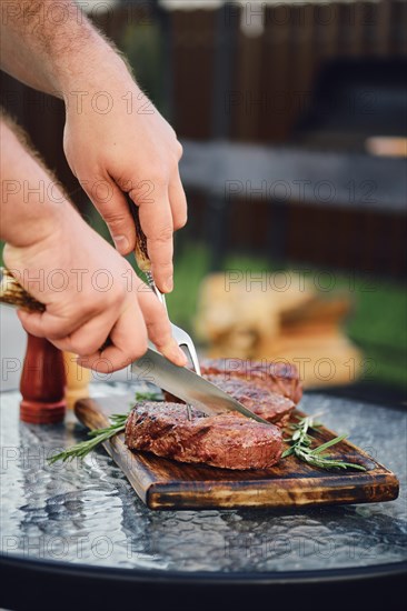 Unrecognizable man cutting freshly grilled beef steak on backyard