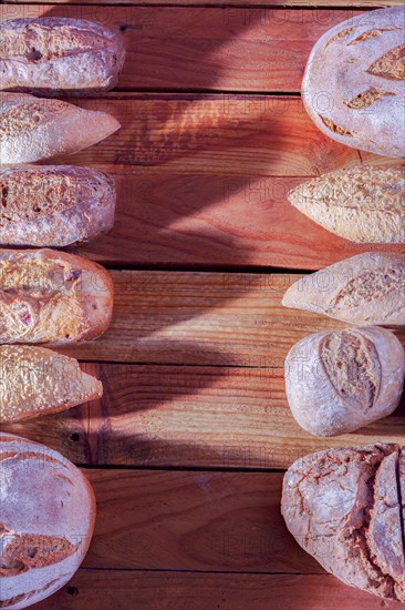 Different types of loaves and loaves of rustic artisan bread in a row on a wooden table with a copy space in the center