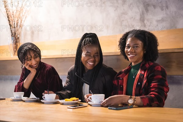 Portrait of three cheerful multicultural friends drinking coffee in a cafeteria