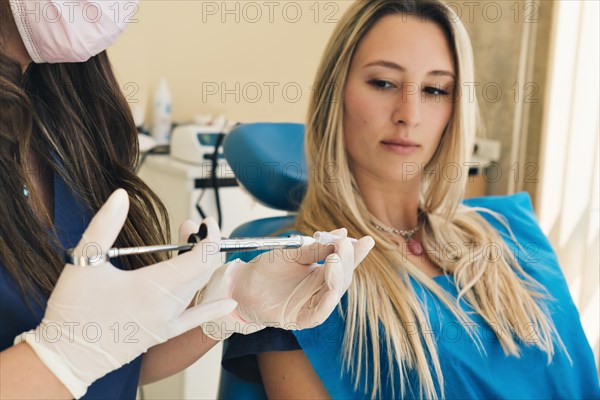 Dentist prepares anesthesia in dental office in background patient looks at injection with trepidation. Selective focus