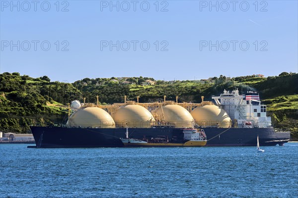 LNG or liquified natural gas tanker moored by industrial pier and green hill on sunny day. Alternative gas supply